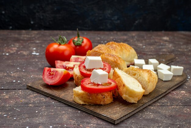 Свежий вкусный хлеб, длинная булочка, вид спереди, в форме нарезанного теста с сыром и помидорами на коричневом