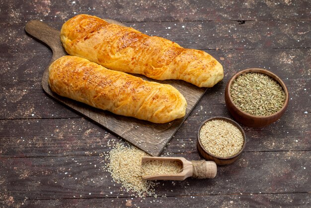 Front view of fresh tasty pastry long bun formed pastry with seasonings on the brown wooden desk