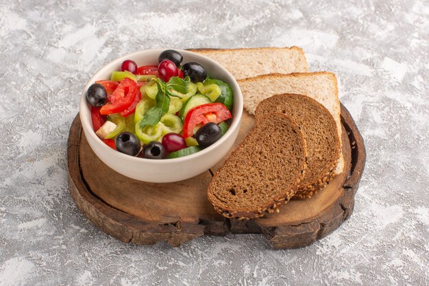 Front view fresh vegetable salad with sliced cucumbers tomatoes olive and white cheese inside plate with bread on the grey desk vegetable food salad meal