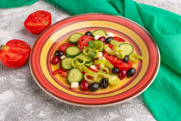 Front view fresh vegetable salad with sliced cucumbers tomatoes olive and white cheese inside plate with tomatoes on the grey surface vegetable food salad meal snack