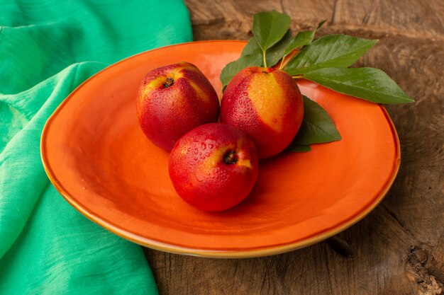 Вид спереди свежие целые персики внутри оранжевой тарелки на деревянном столе