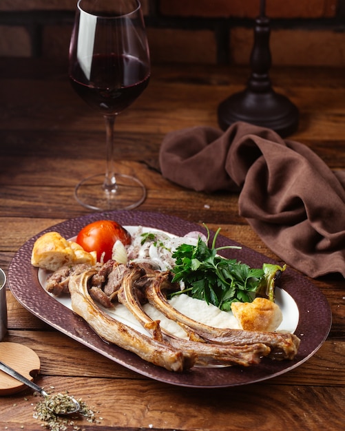 A front view fried meat bones with greens and tomato on the brown wooden desk meal food meat