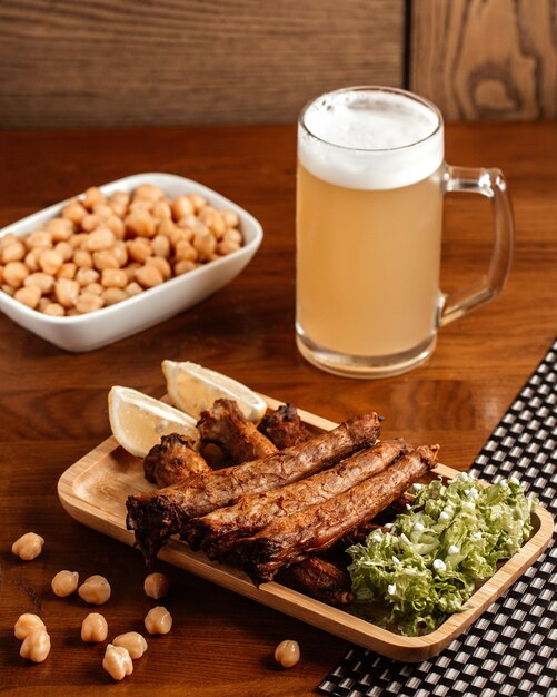 Вид спереди жареное мясо с пивом, лимоном и фасолью на коричневом деревянном столе.