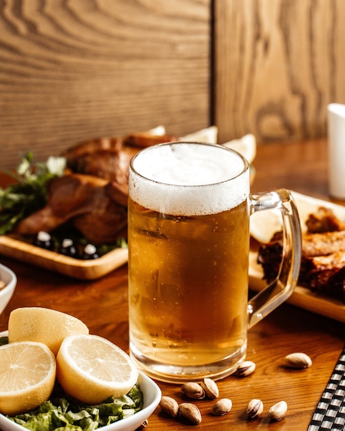 Вид спереди жареное мясо с пивом, лимоном и орехами на коричневом деревянном столе.
