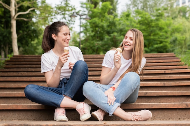 Free photo front view friends sitting on stairs while eating ice cream