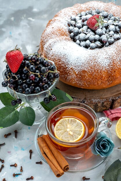 A front view fruit cake with fresh blue,berries and along with cup of tea on bright, cake biscuit sweet sugar