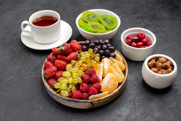 Vista frontale della composizione nella frutta diversi frutti freschi con una tazza di tè sulla scrivania grigio scuro