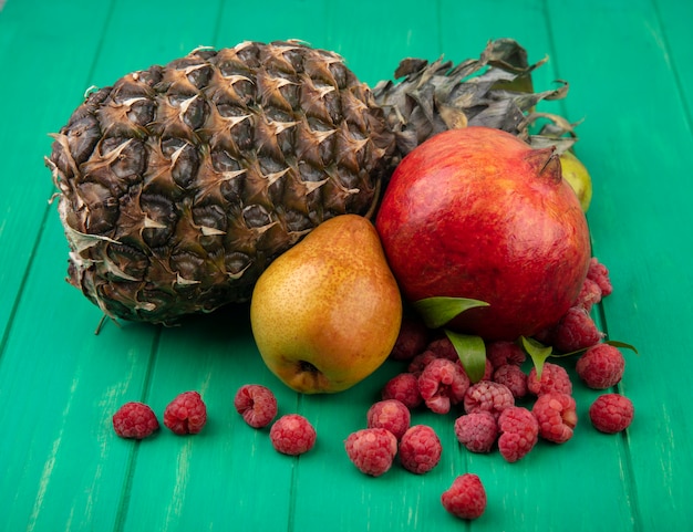 Front view of fruits as pineapple peach pomegranate and raspberries on green surface