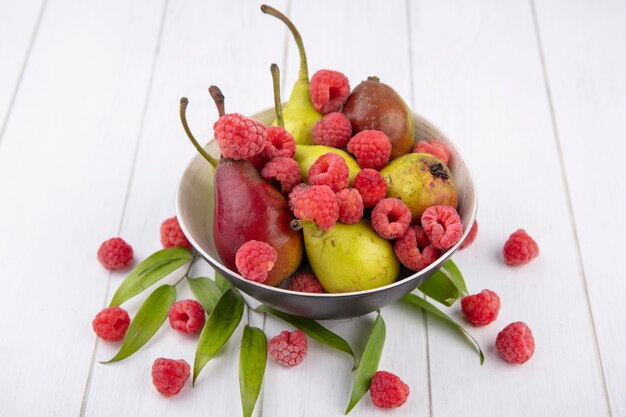 Front view of fruits as raspberry and peach in bowl with leaves on wooden surface