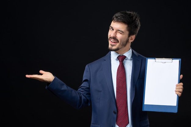 Vista frontale di un adulto divertente in tuta che tiene spazio libero per scrivere e puntare qualcosa sul lato destro su un muro scuro isolato