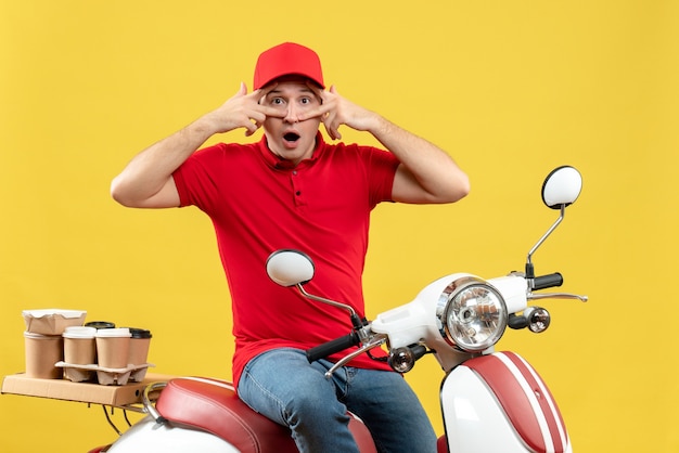 Front view of funny and emotional young guy wearing red blouse and hat delivering orders on yellow background