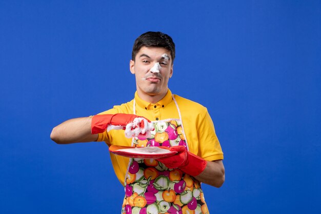 Front view funny housekeeper with foam on his face washing plate on blue space