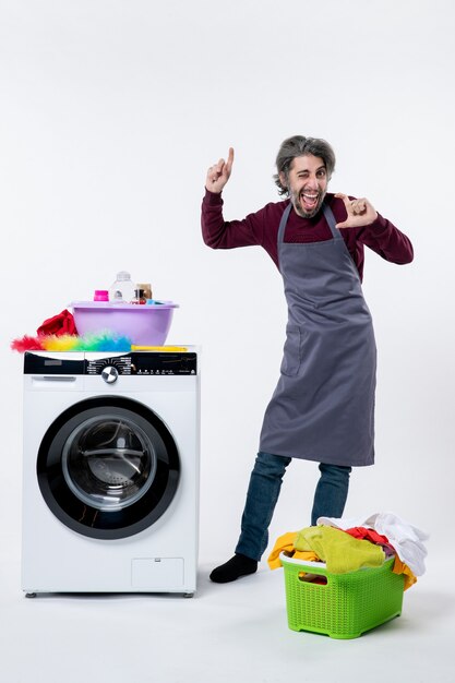 Front view funny joyful man standing near washer laundry basket on white background