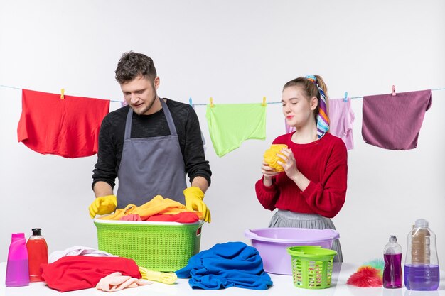 Front view funny young couple man holding laundry basket and wife holding bath sponge on white wall