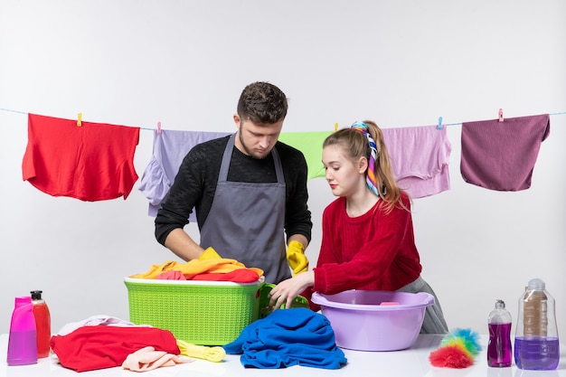 Front view funny young couple sorting clothes on white wall