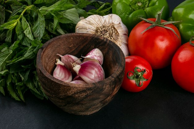 Front view of garlic in a bowl with tomatoes and mint on a black surface