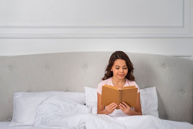 Front view girl on bed reading time