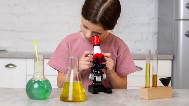 Front view of girl doing experiments with microscope and test tubes