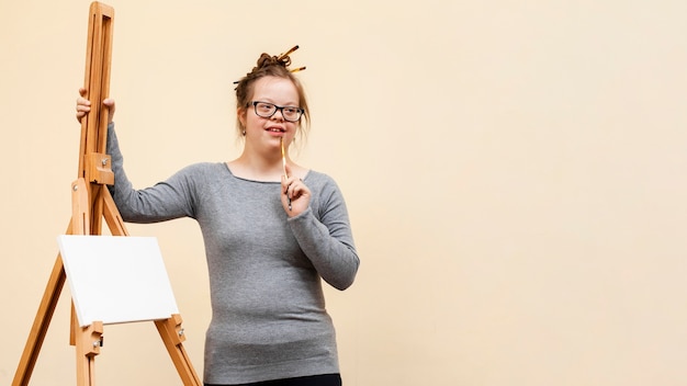 Front view of girl down syndrome posing next to easel