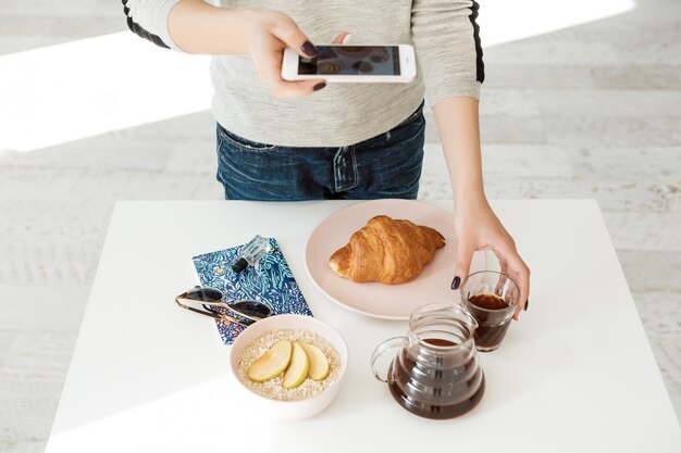 Front view of girl holding phone while shooting tasty breakfast.