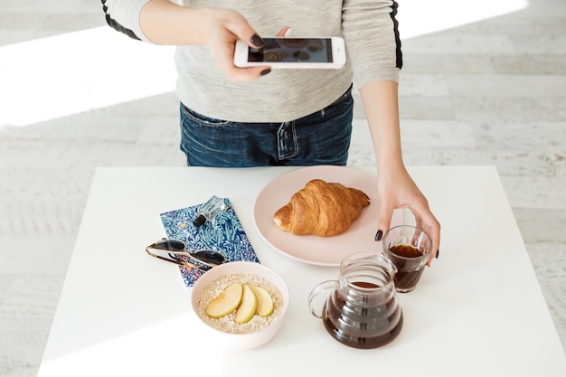 Front view of girl holding phone while shooting tasty breakfast.