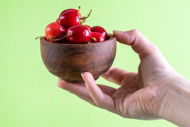 Front view the girl holds in her hand cherries in a wooden bowl on light green