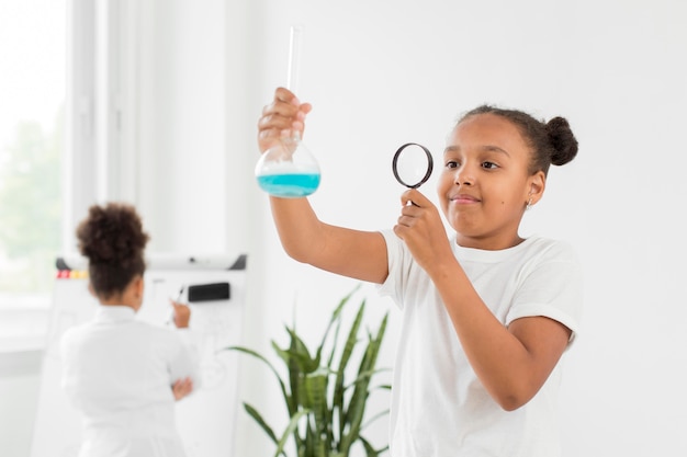 Front view of girl looking at potion in tube with magnifying glass