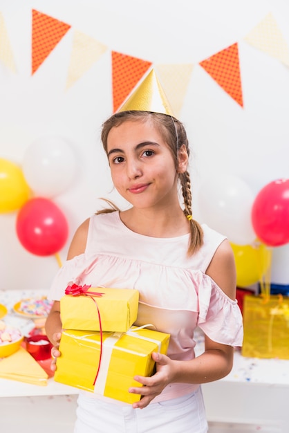 Front view of girl in party hat holding gifts in birthday party