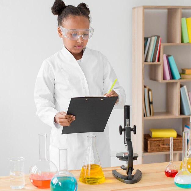 Vista frontale della ragazza scienziata con camice da laboratorio e blocco note