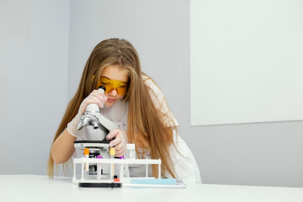 Front view of girl scientist with safety glasses and microscope