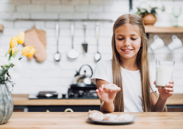 Foto gratuita ragazza di vista frontale che prende un biscotto e che tiene un bicchiere di latte