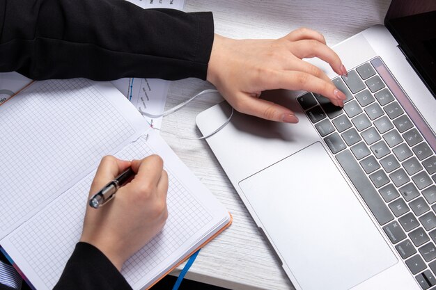 A front view girl taking notes writing down notes in front of table with schedules and graphics and using laptop job business activity