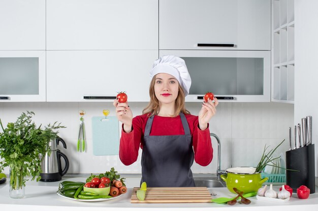 Front view glad female cook in apron holding tomatoes