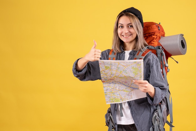 Front view of glad traveler woman with backpack holding map giving thumbs up