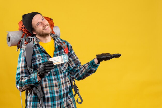 Front view of glad young backpacker with black hat holding plane ticket