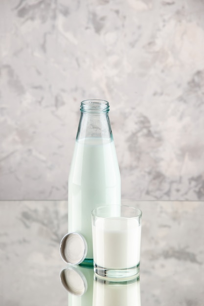 Free photo front view of glass bottle and cup filled with milk cap on white smoke background with free space