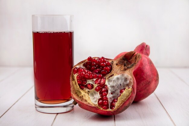 Front view glass of pomegranate juice with pomegranates on white wall