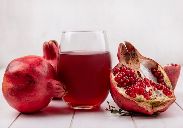 Front view glass of pomegranate juice with pomegranates on white wall