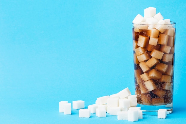 Front view of glass of soft drink with sugar cubes and copy space