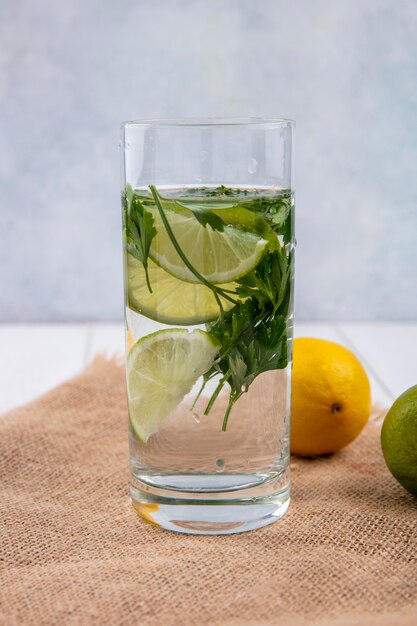 Front view of glass of water with greens and lime on a beige napkin