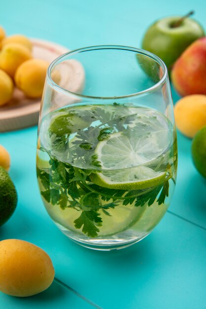 Free photo front view of glass of water with greens and lime on a blue surface