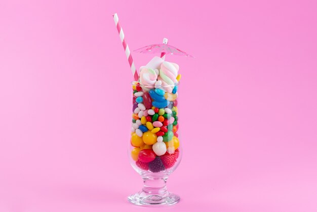 A front view glass with candies and confitures on pink, sweet color rainbow