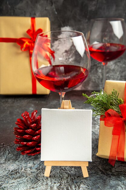 Вид спереди бокалы вина рождественские подарки белый холст на деревянном мольберте на темноте