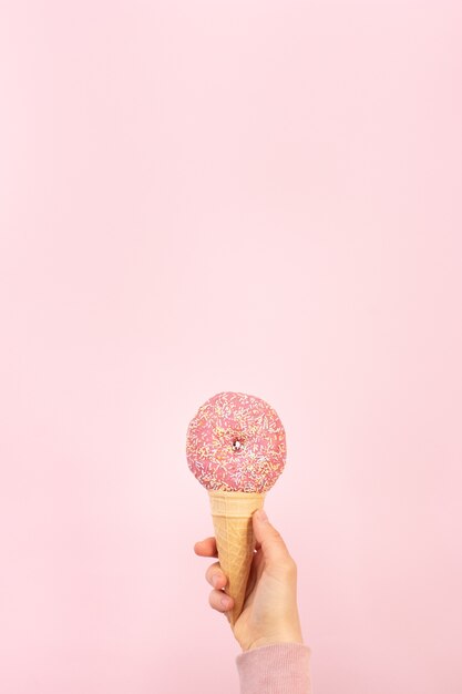 Front view of glazed doughnut with sprinkles in ice cream cone with copy space
