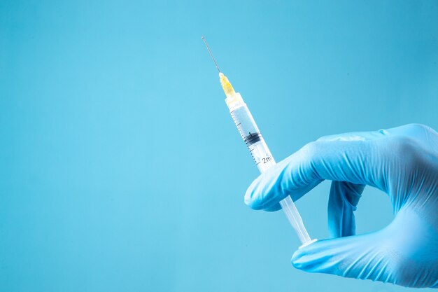 Front view of glove wearing hand holding full syringe on blue wave background