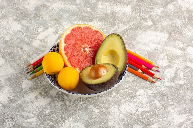 Front view grapefruits and avocado inside plate with pencils on white surface