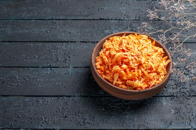 Салат из тертой моркови, вид спереди, внутри тарелки на темно-синем деревенском столе здоровый салат цвет спелых диетических овощей