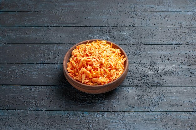 Салат из тертой моркови, вид спереди, внутри тарелки на темно-синем деревенском столе салат цвета спелых здоровых диетических овощей