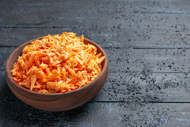 Салат из тертой моркови, вид спереди, внутри тарелки на темно-синем деревенском столе салат цвета спелых здоровых диетических овощей