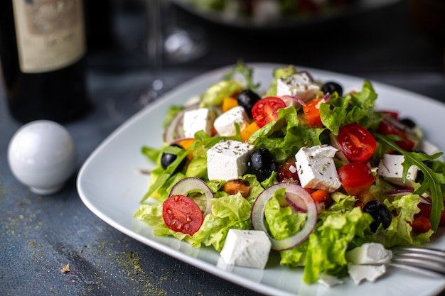 正面のギリシャ風サラダスライスした野菜のサラダトマトきゅうりのホワイトチーズと白いプレートビタミン野菜の中のオリーブ
